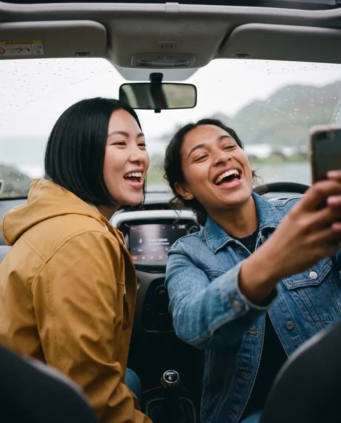 Maya and Alex laughing and singing in a car on a rainy road trip